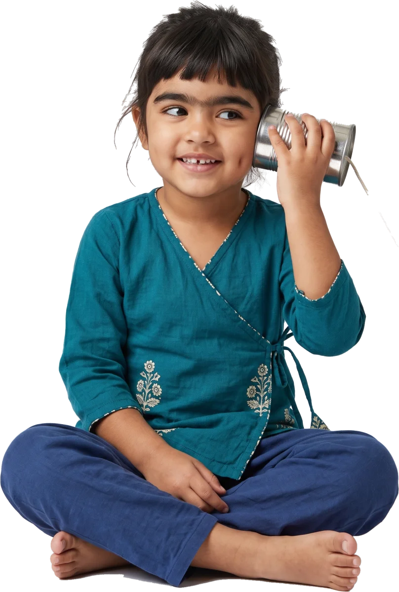 A girl sitting cross-legged, holding a tin can to her ear like a telephone and smiling.
